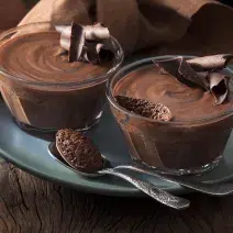 Foto de dos tazones pequeños con mousse de chocolate adentro encima de un plato azul Foto de dos tazones pequeños con mousse de chocolate adentro encima de un plato azul